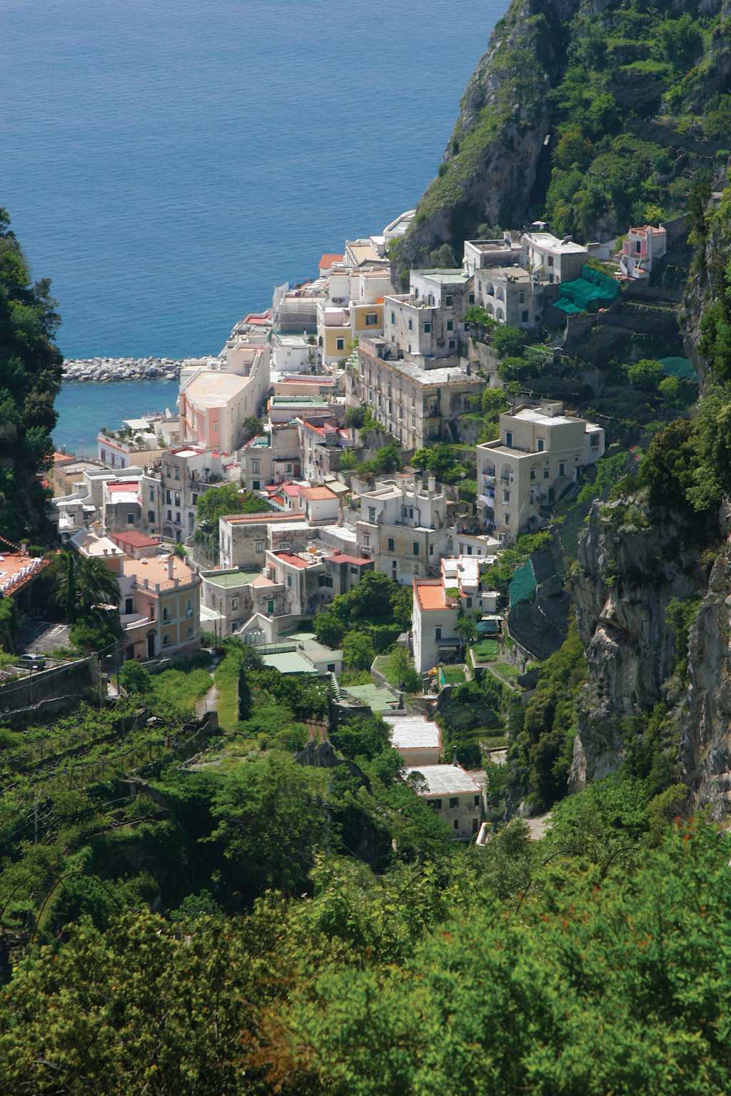 A picturesque coastal town nestled among lush greenery, with colorful buildings cascading down the hillside and overlooking the serene blue waters of the sea.