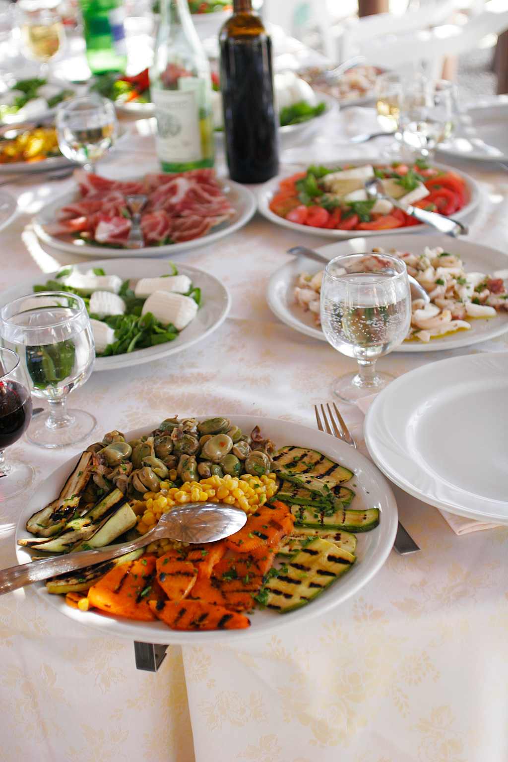 A table filled with a variety of appetizing dishes, including grilled vegetables, cured meats, and various salads, accompanied by glasses of wine, creating a visually appealing and inviting dining experience.