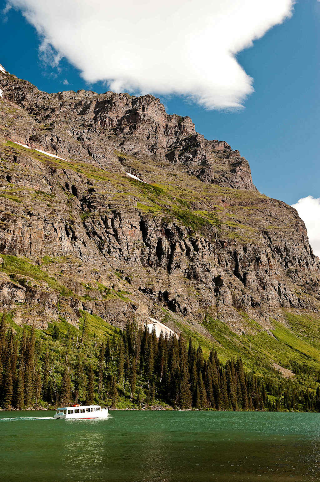 A scenic landscape with a serene green lake surrounded by rugged, snow-capped mountains and a forested area in the foreground.