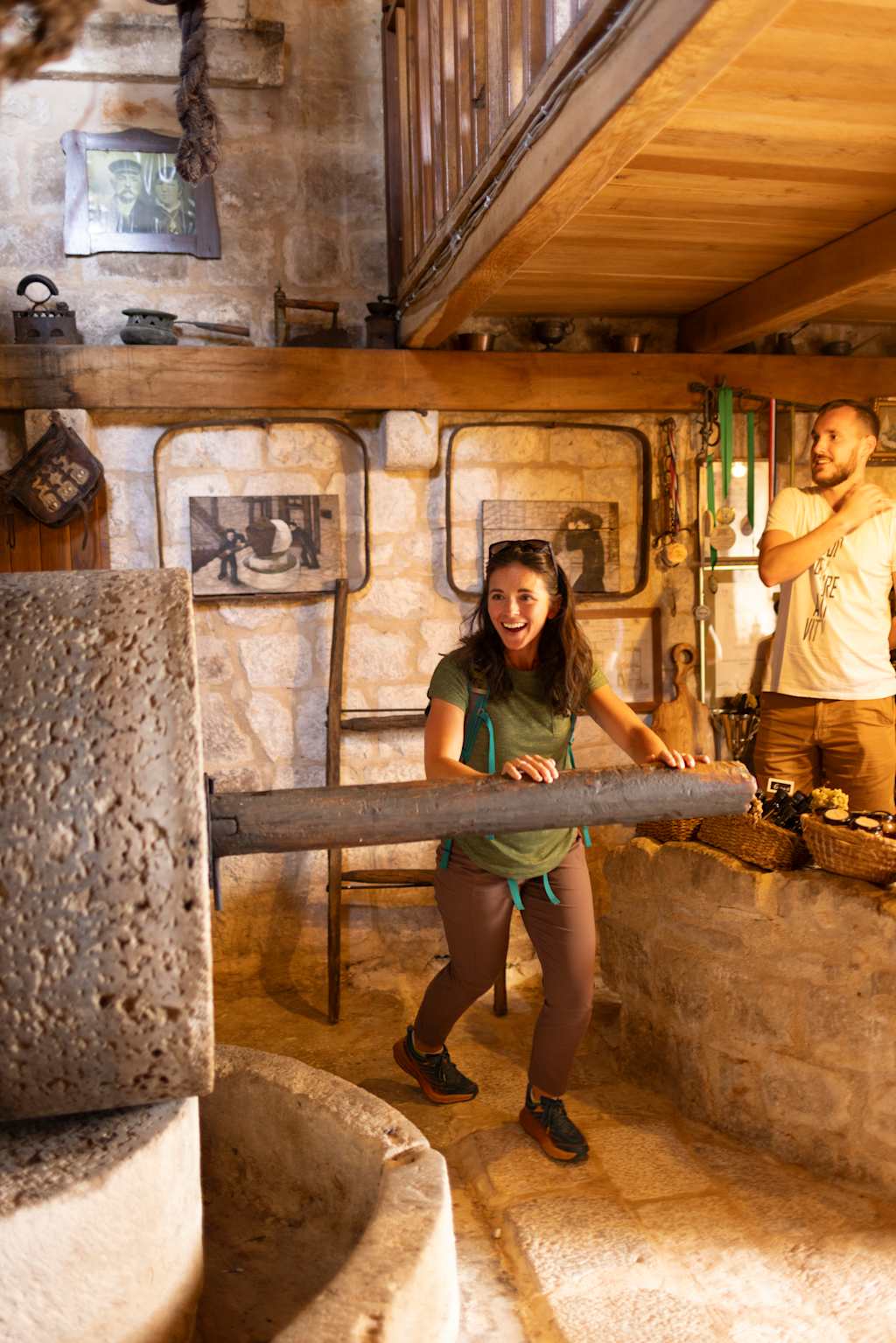 A person sitting on a wooden bench in a rustic cabin interior, surrounded by various household items and furnishings.