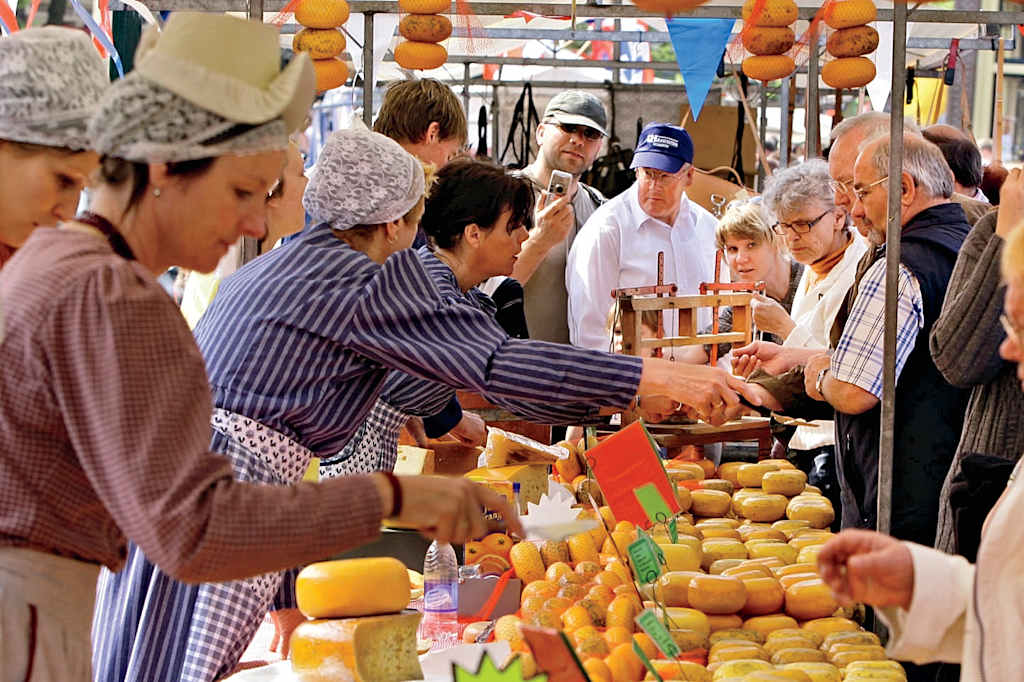 A bustling outdoor market with vendors selling various fruits and vegetables, surrounded by a crowd of people browsing and purchasing the goods.