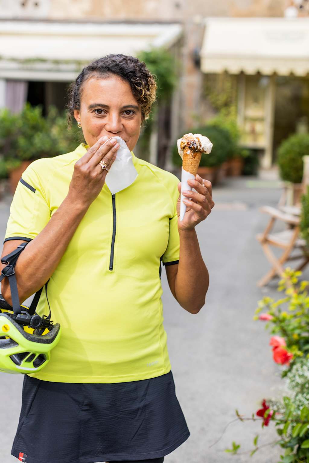 A woman in a bright yellow shirt is holding an ice cream cone and appears to be in a garden setting with flowers and other greenery in the background.