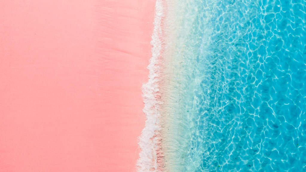 A vibrant pink beach meets the crystal-clear turquoise waters, creating a visually striking contrast.
