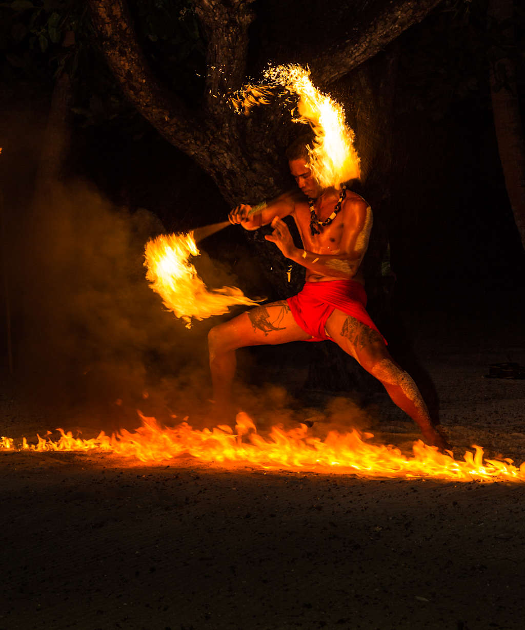 A person in a red costume is performing a fire-breathing act, surrounded by flames on a dark background.