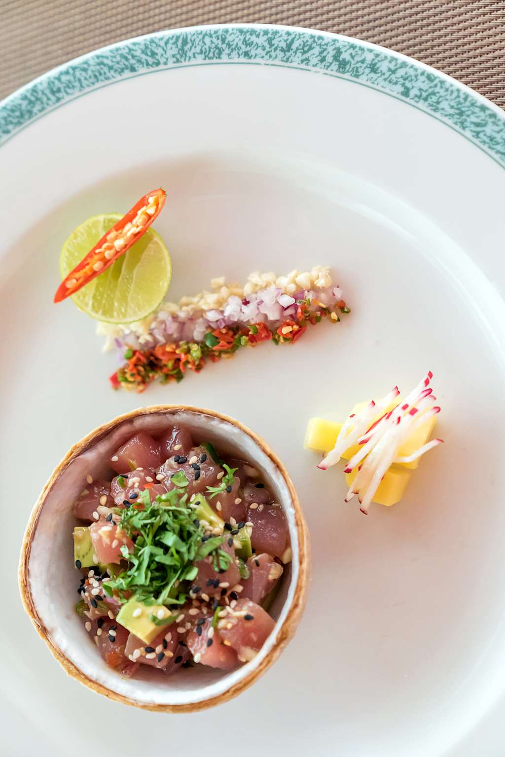A white plate with a variety of Mexican-inspired dishes, including a bowl of what appears to be a red bean or chili dish, a lime wedge, and what looks like a spicy salsa or relish on the side.