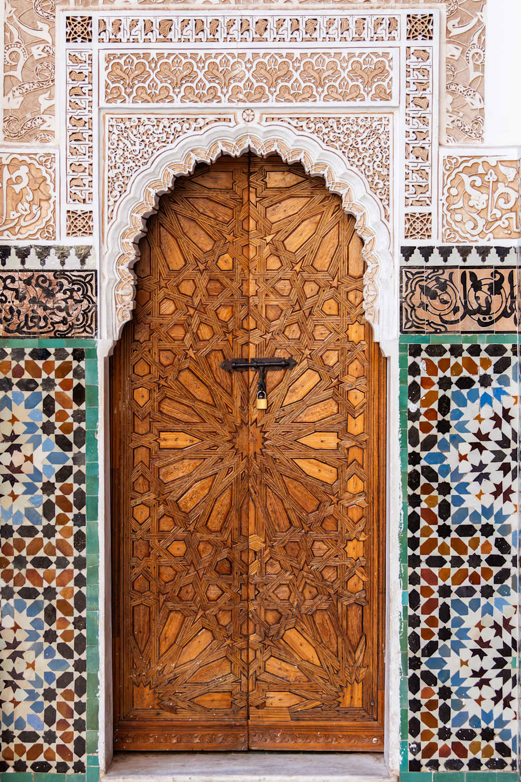 A beautifully ornate wooden door with intricate carvings and patterns, set against a backdrop of colorful mosaic tiles, creating a visually striking architectural feature.