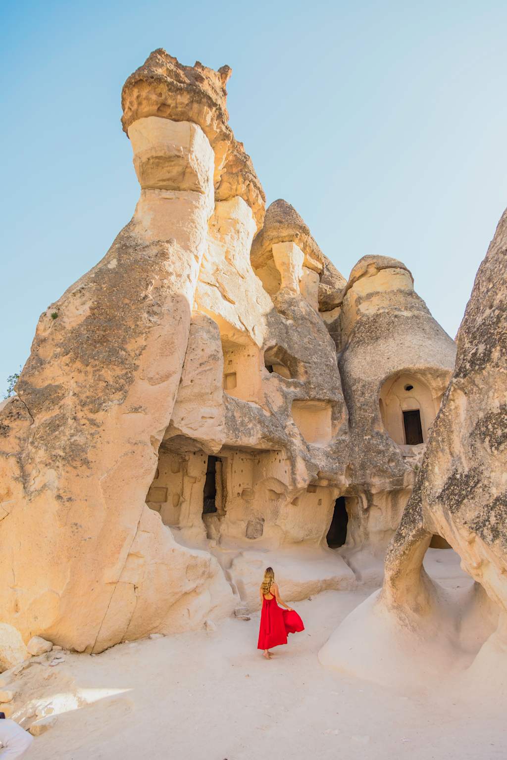 The image depicts a person wearing a red dress standing in front of large, unique rock formations in a desert-like landscape.