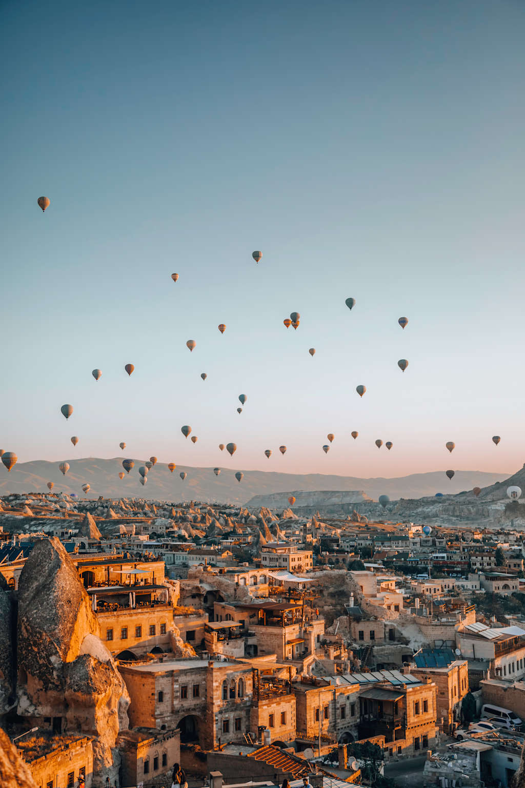 A picturesque cityscape with a stunning array of hot air balloons floating against a vibrant sky, overlooking the rooftops and buildings of the historic town below.