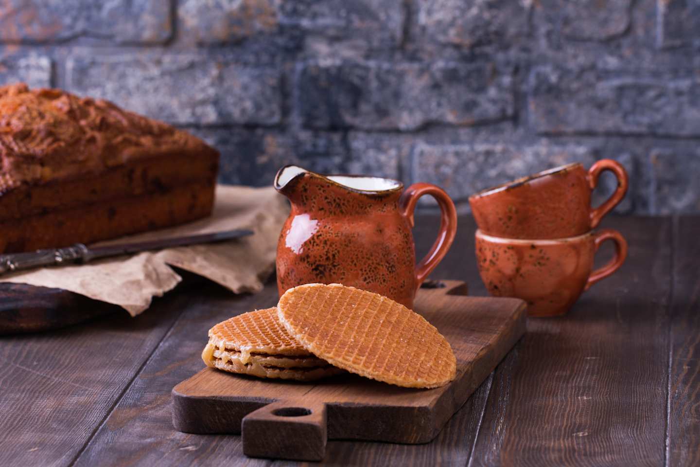 Stack of Stroopwafels or Dutch Waffles with caramel. Traditional Dutch dessert Stroopwafels cake with cups of coffee and milk. Rustic wooden table.