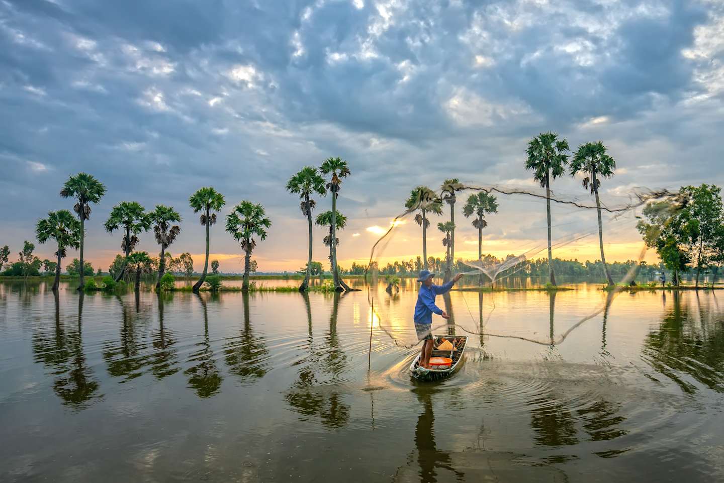 An Giang, Vietnam - September 13, 2018: Unidentified fishers throw fish net to catch fish a lake in the morning when sunrises behind every palm tree adorn beauty of rural areas in An Giang, Vietnam.
