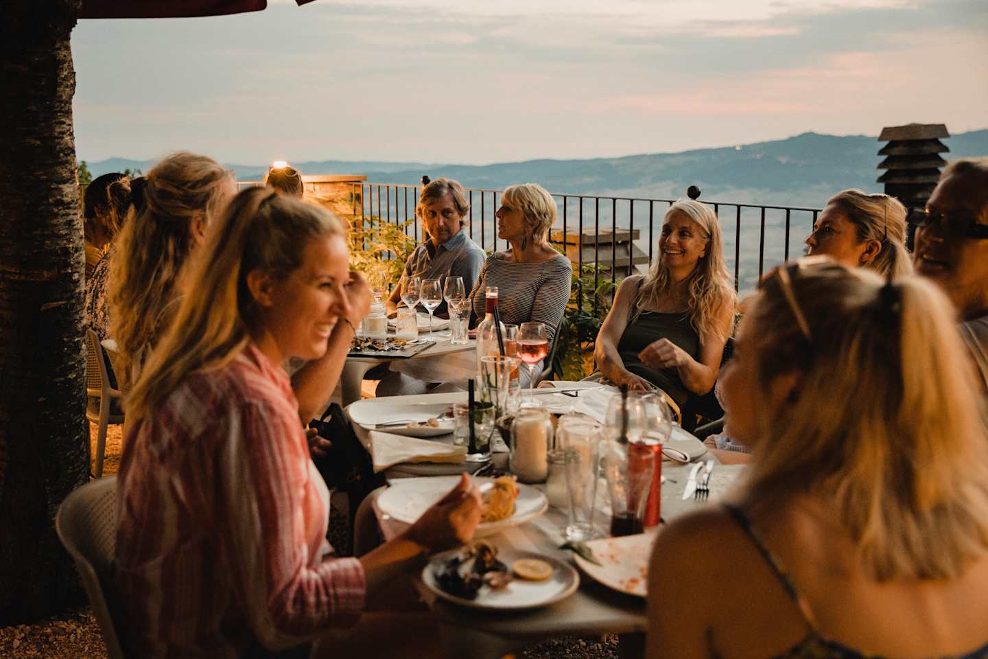 Large group of people enjoying an Italian meal together on top of a rooftop restaurant.