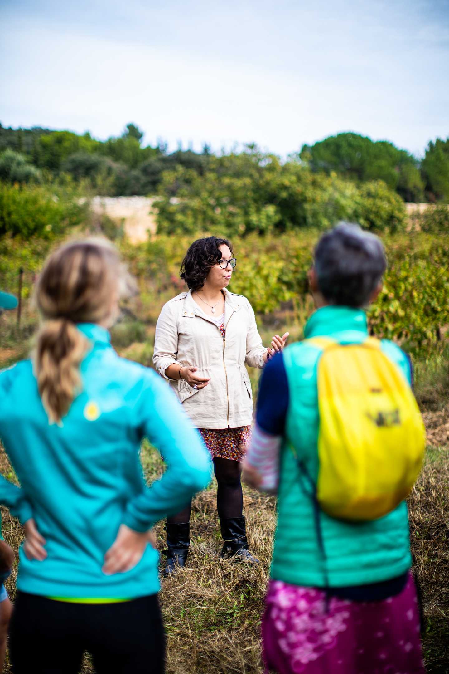 A group of people, likely students or volunteers, are standing in a lush, green outdoor setting, engaged in what appears to be a discussion or activity.