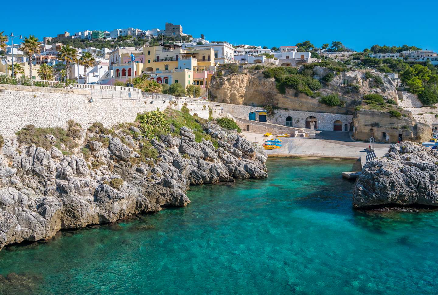 A picturesque coastal town nestled on rocky cliffs, with vibrant white and colorful buildings overlooking a stunning turquoise bay.