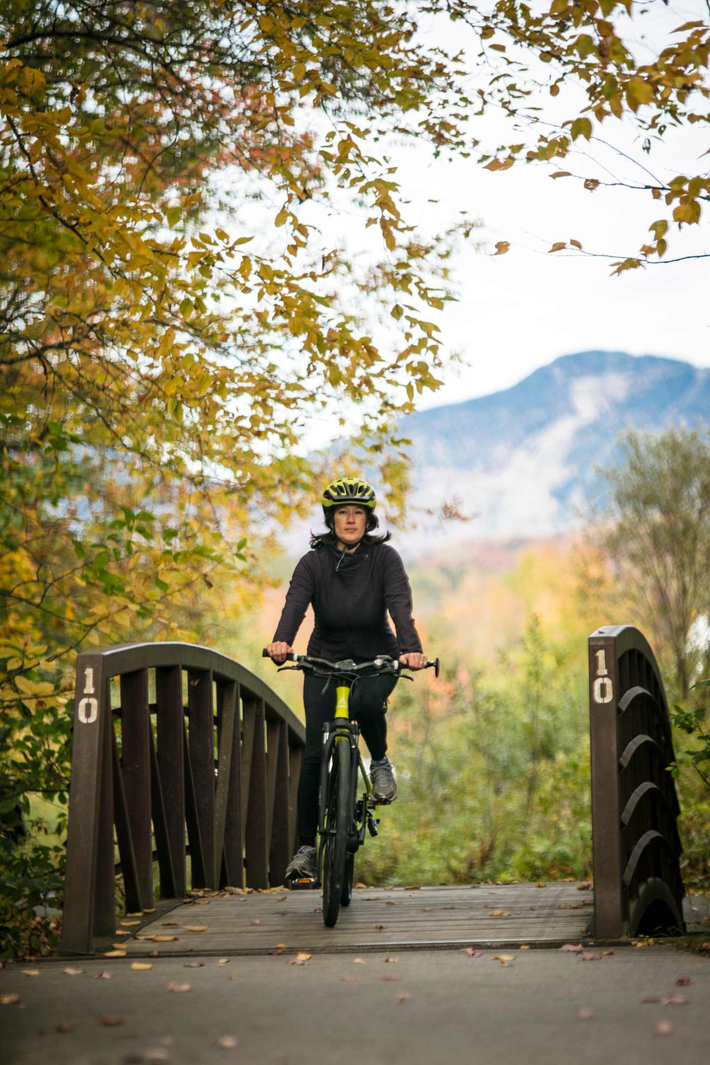 VBT Fall 2019 Photoshoot Single guest biking over bridge on Stowe bike path with mountains in the background  by JAM Creative