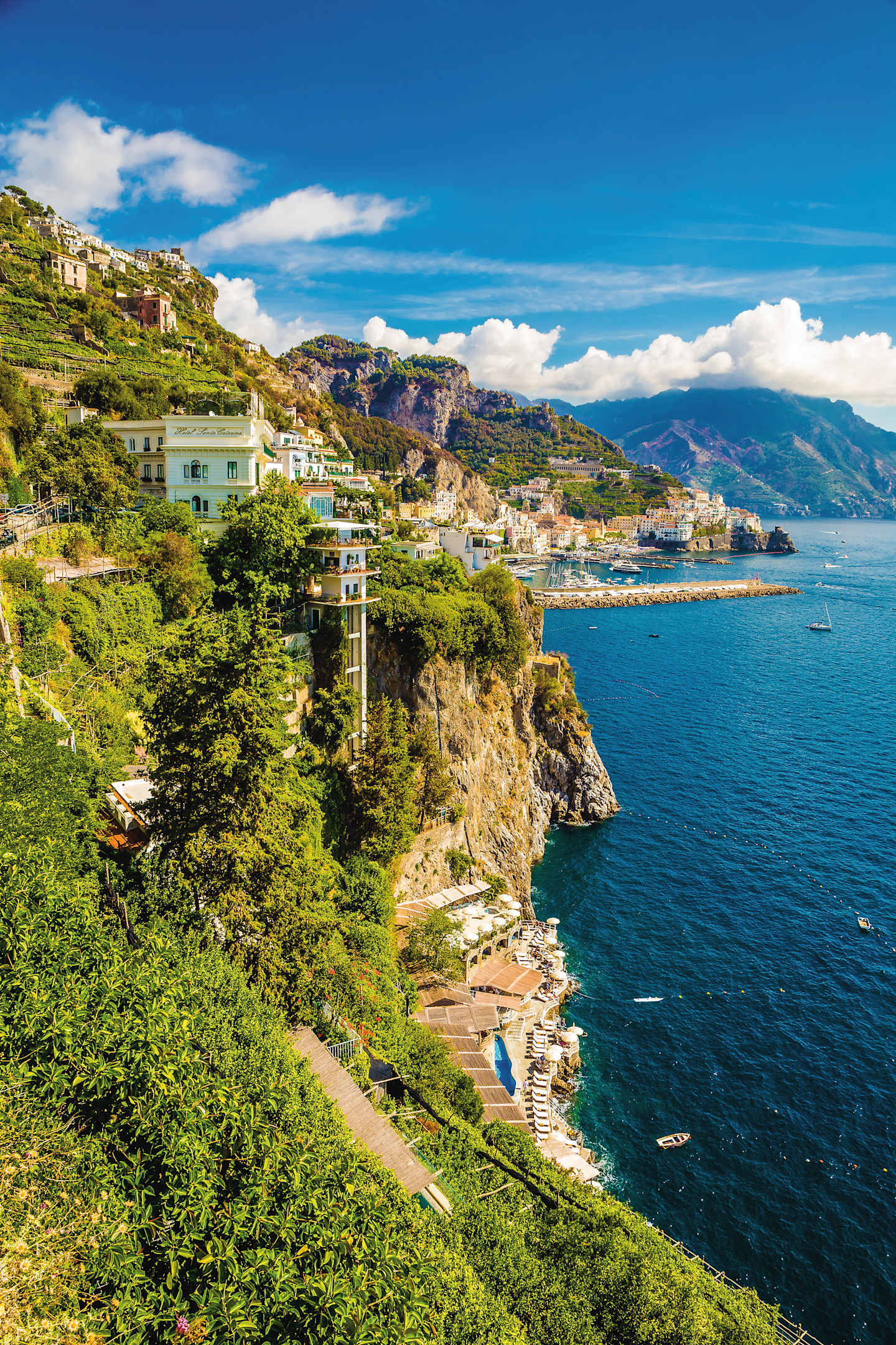A picturesque coastal town nestled among lush greenery, with colorful buildings cascading down the hillside and a serene blue sea stretching out in the background.