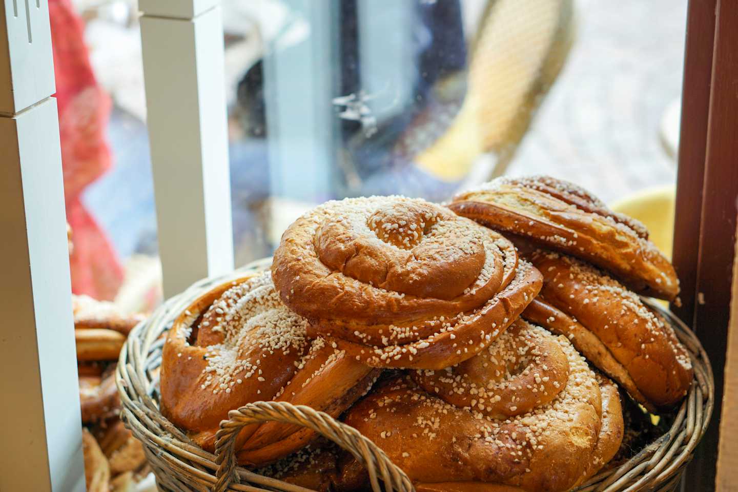 A basket filled with freshly baked, golden-brown cinnamon rolls dusted with powdered sugar, set against a blurred background of other baked goods.