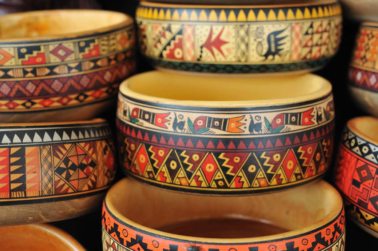 Colorful, patterned ceramic bowls or containers with intricate geometric and tribal designs, arranged in a stack.