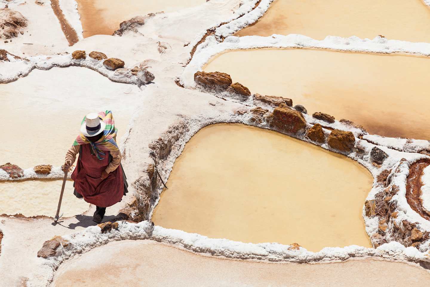 A person in traditional Tibetan clothing stands in a snowy, mountainous landscape, with rocky formations and a warm-toned sky in the background.