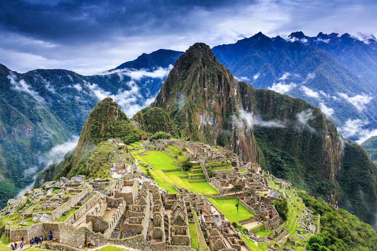 A breathtaking view of the ancient Inca ruins of Machu Picchu nestled amidst the towering, lush green mountains and dramatic cloudy skies in the background.
