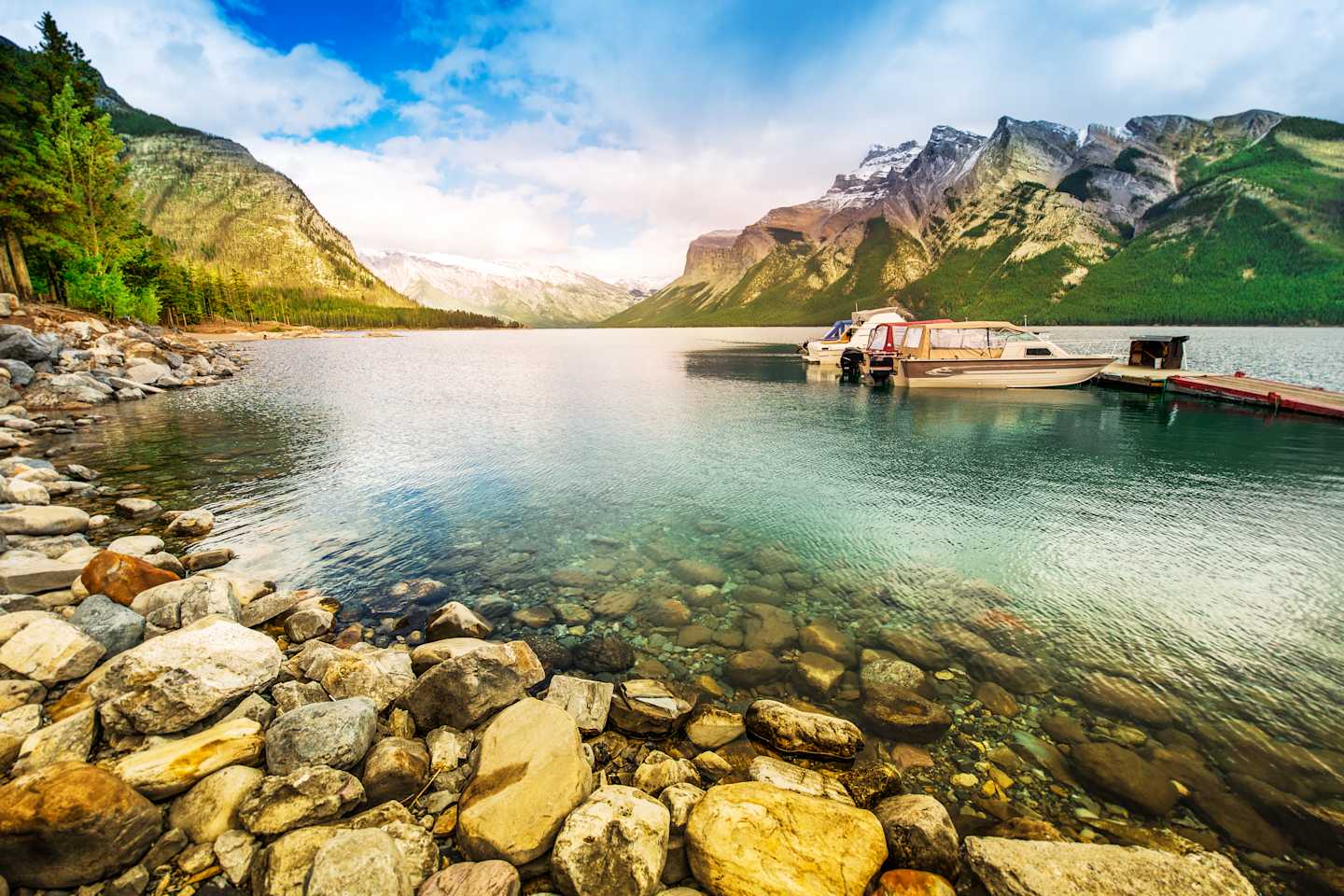 A serene alpine lake surrounded by majestic mountains, with a small boat dock in the foreground and a clear, reflective surface in the water.