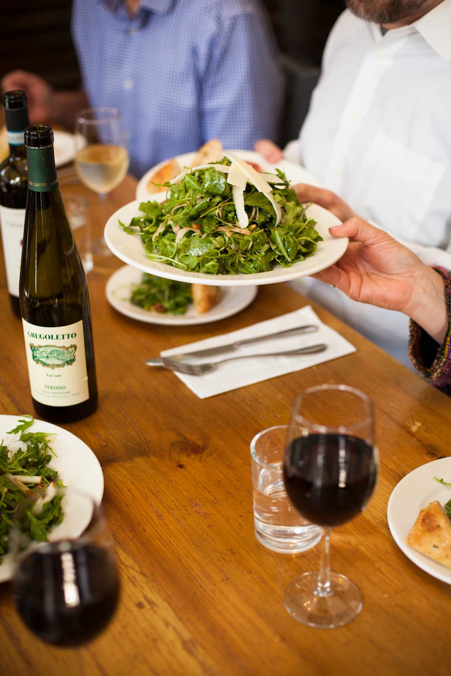 A plate of fresh salad with a glass of red wine and other dining items on a wooden table.