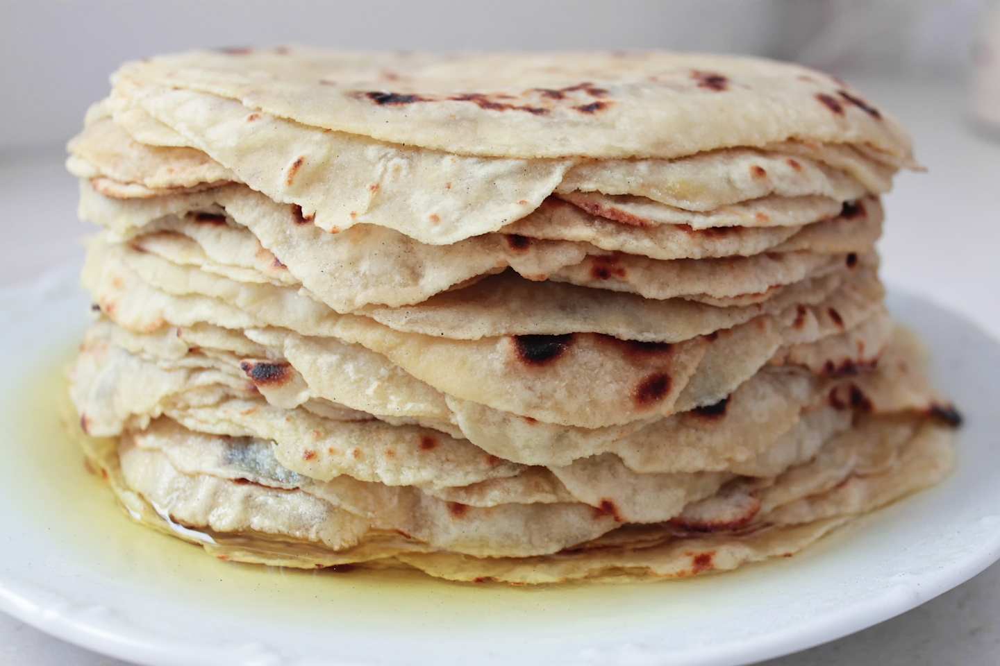 A stack of freshly baked pita breads sits on a white plate against a plain background.