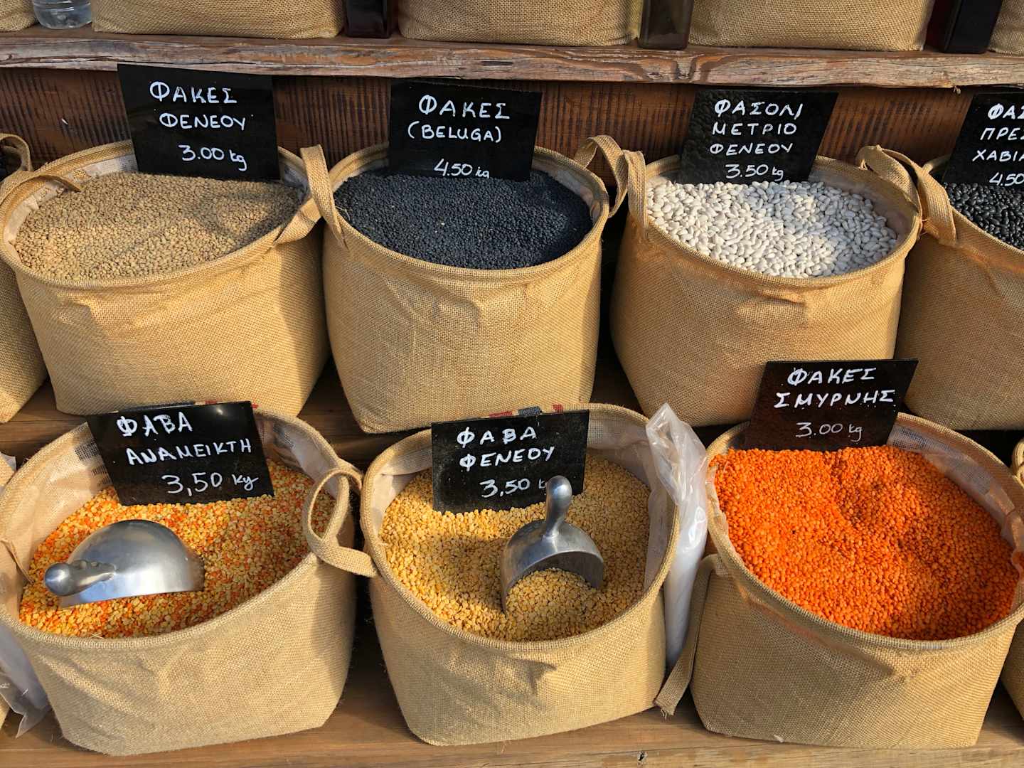 Various types of grains and spices are displayed in burlap sacks, with labels indicating their names and prices.
