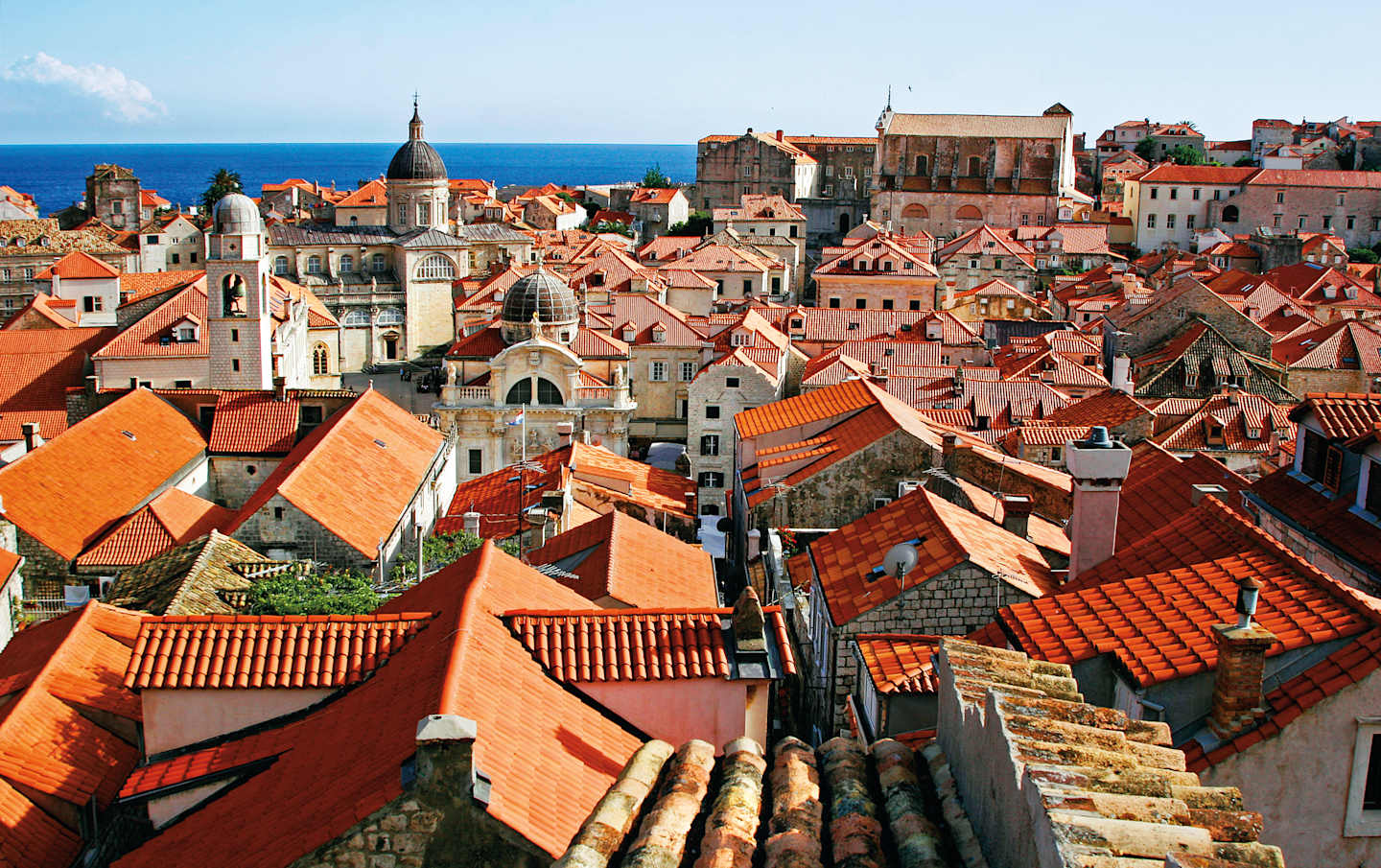 A vibrant cityscape with a sea of terracotta roofs, spires, and historic buildings nestled against a backdrop of a clear blue sky.