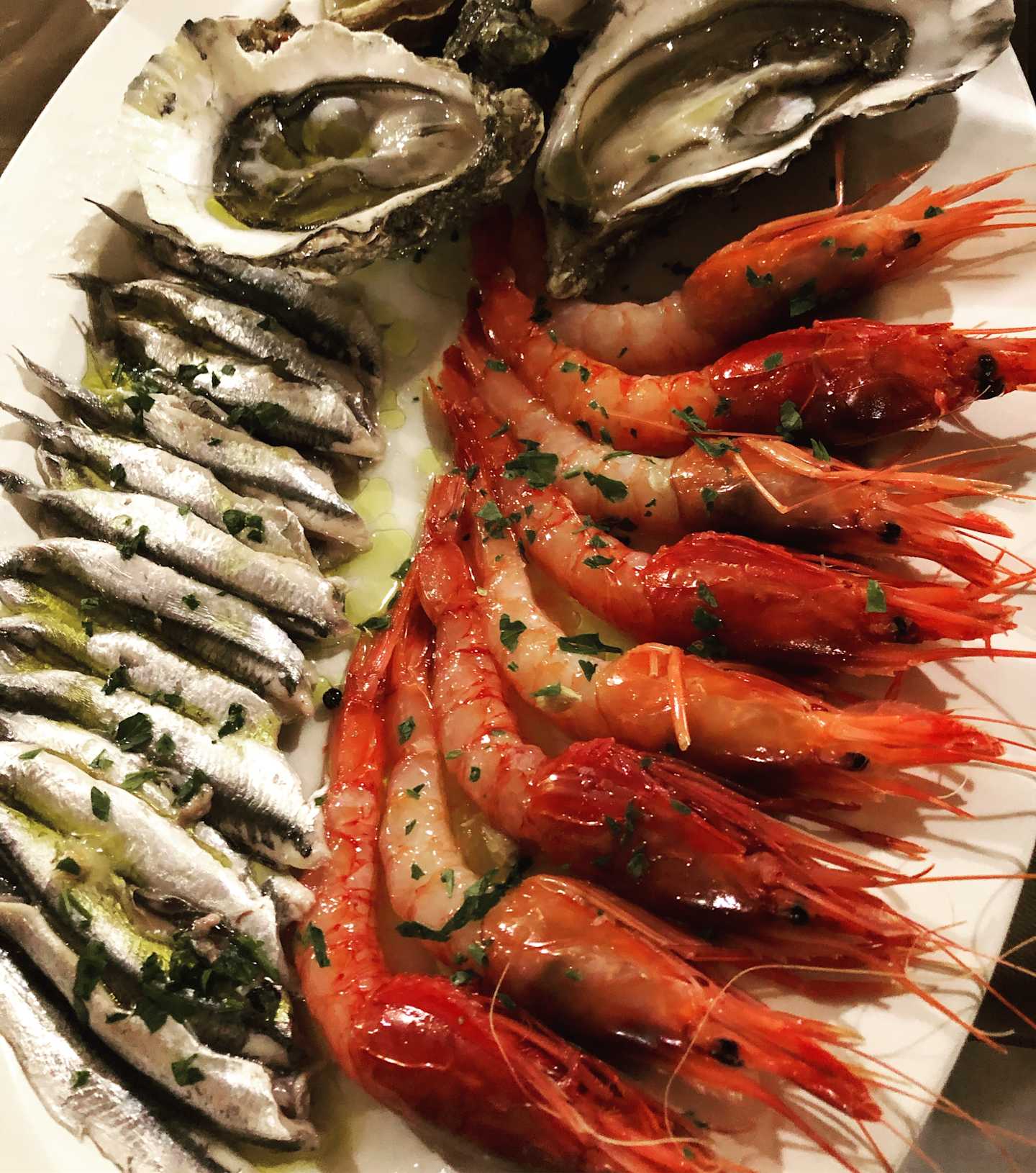 A plate filled with various seafood delicacies, including grilled sardines, juicy shrimp, and freshly shucked oysters, arranged in an appetizing display.