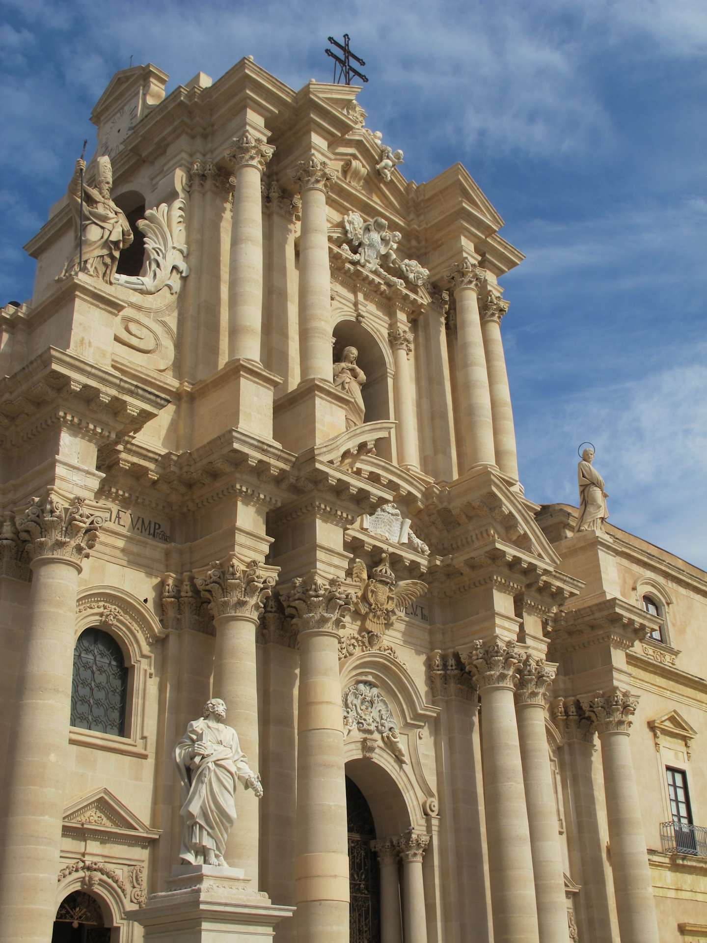 A grand, ornate cathedral with intricate architectural details and statues adorns the foreground, set against a bright blue sky in the background.
