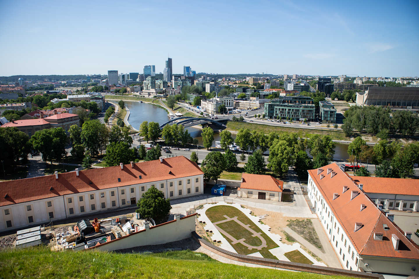 A panoramic view of a vibrant city skyline, with a mix of modern high-rise buildings and historic structures, surrounded by lush greenery and a winding river in the foreground.