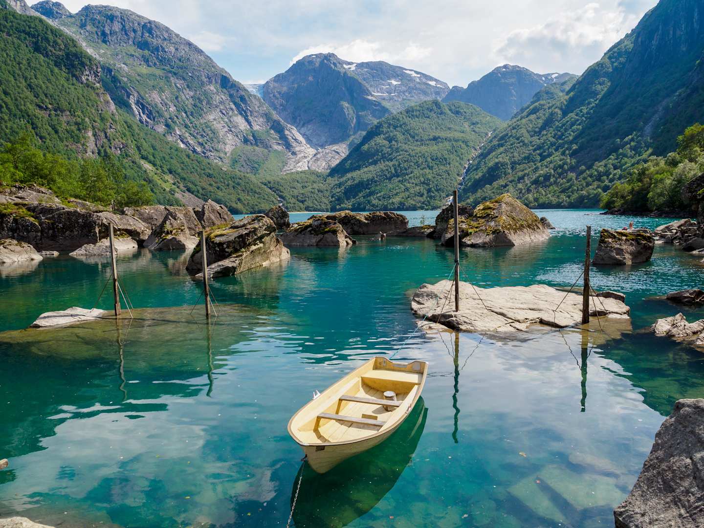 A serene lake surrounded by majestic mountains, with a small wooden boat floating peacefully on the crystal-clear turquoise waters.