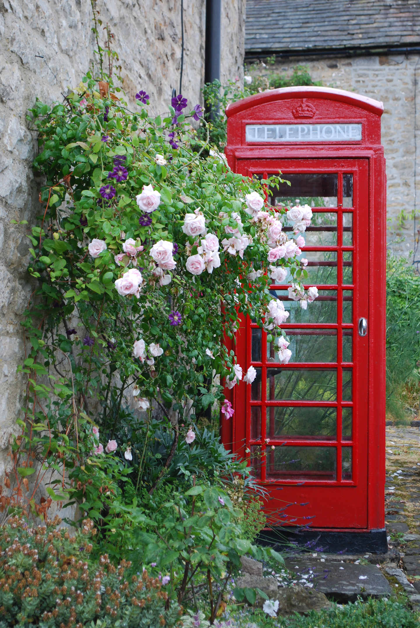 A vibrant red telephone booth stands amidst a lush garden filled with blooming white and purple flowers, creating a charming and picturesque scene.