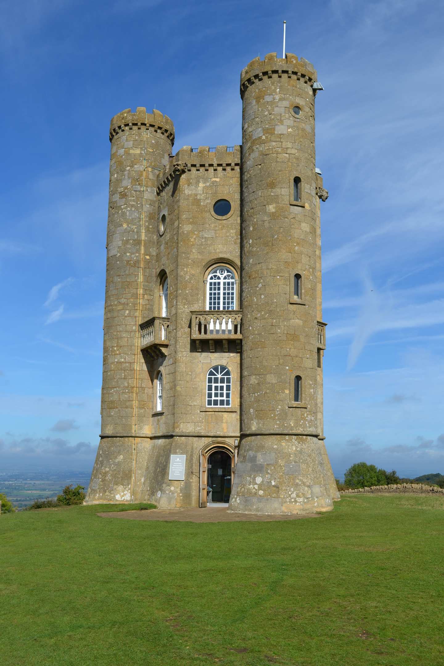 A majestic stone castle with towers and turrets stands on a grassy field, set against a clear blue sky.