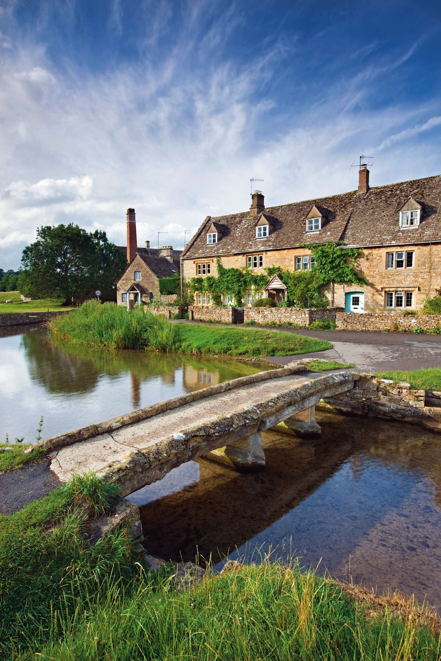 A picturesque village scene with a tranquil pond in the foreground, surrounded by charming stone cottages and lush greenery in the background.