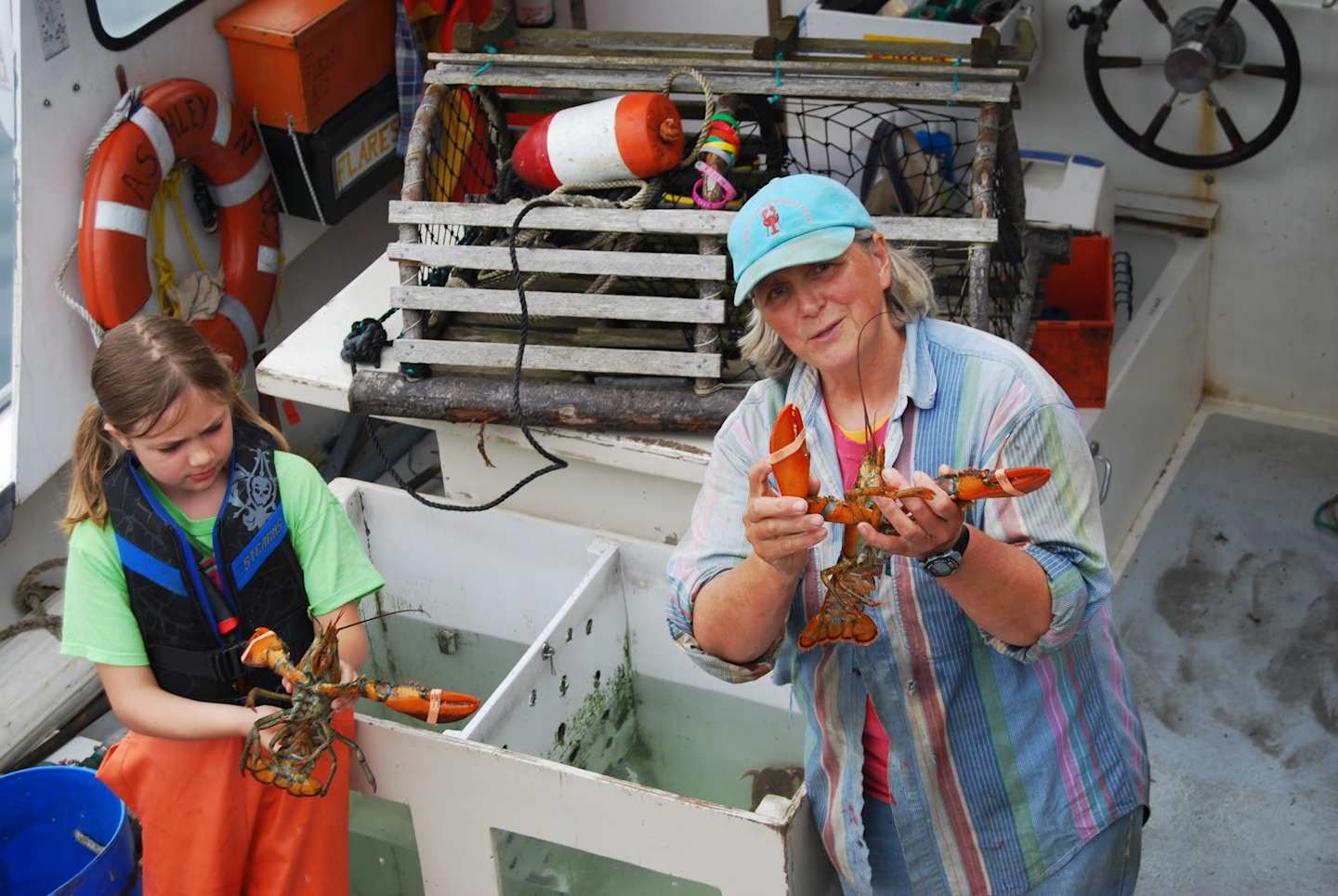Two young women in colorful clothing are working on a project in what appears to be a workshop or garage setting, surrounded by various tools and equipment.