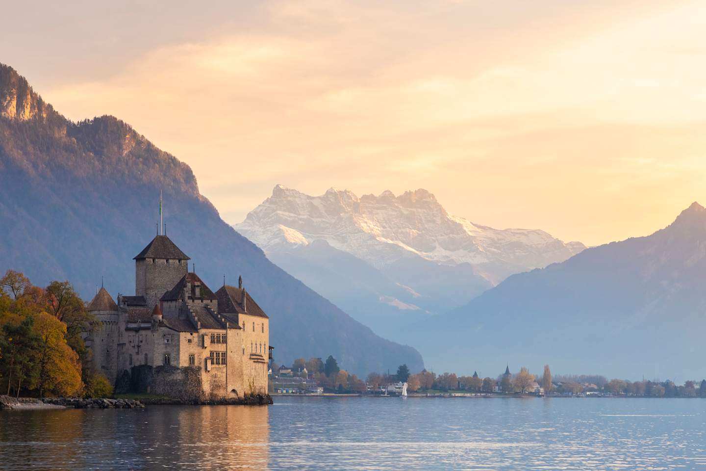A majestic castle stands on the shores of a serene lake, surrounded by towering snow-capped mountains and a vibrant autumn landscape.
