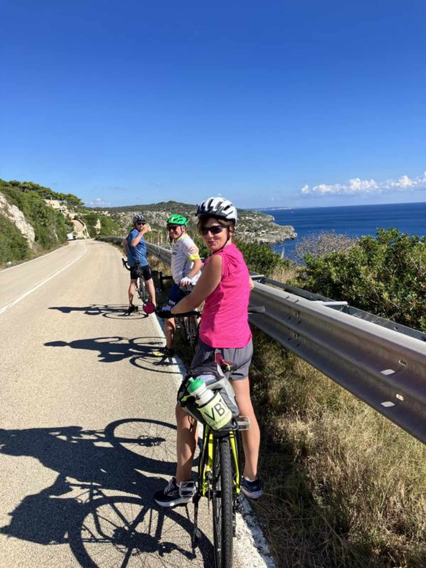 A group of cyclists riding on a coastal road with a scenic ocean view in the background.