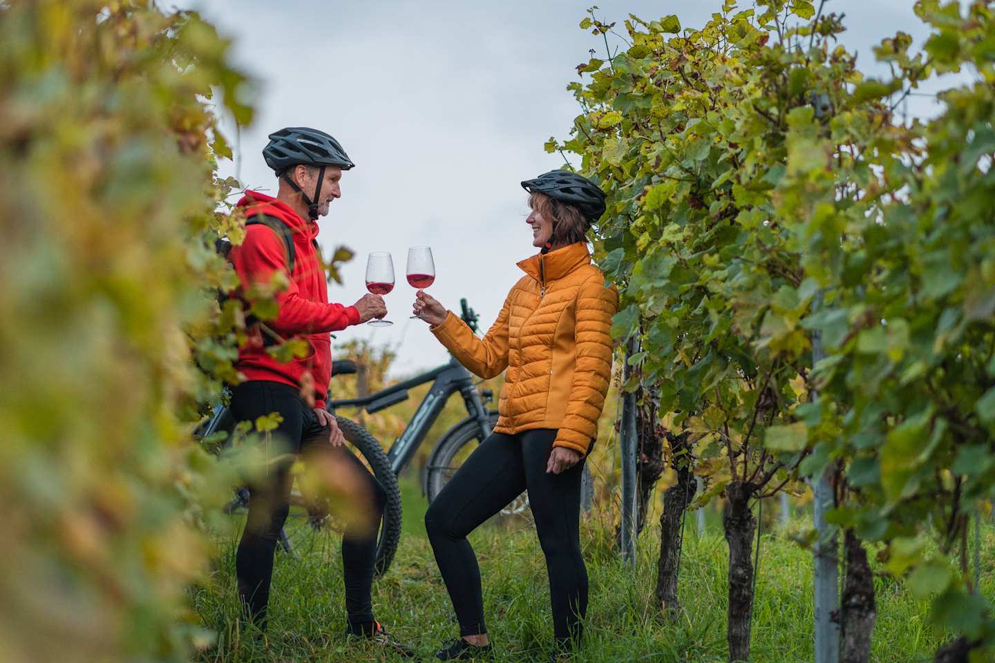 Two people, a man and a woman, standing in a vineyard, holding glasses of wine and enjoying the outdoors.