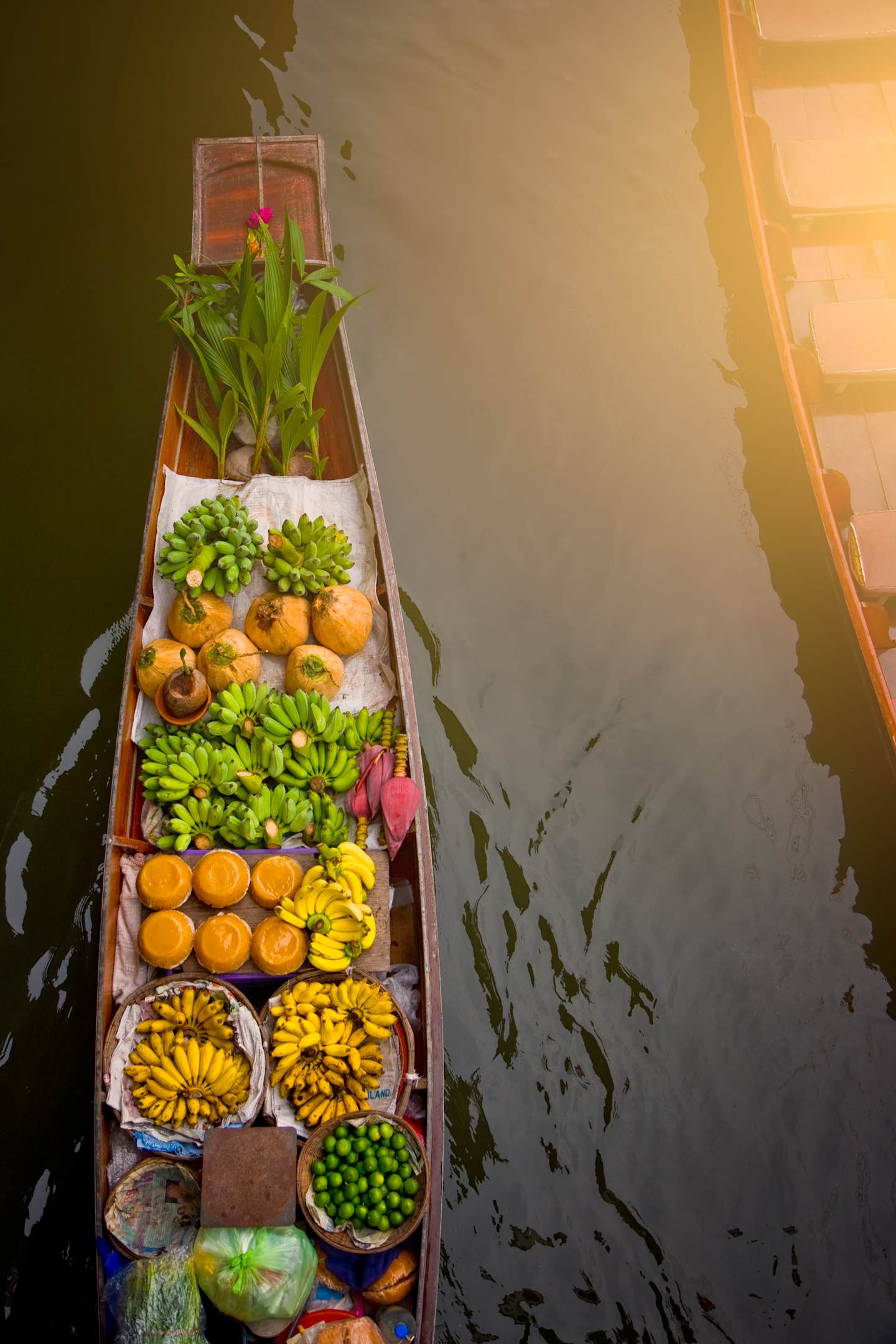 A colorful wooden boat filled with an assortment of fresh fruits and vegetables, floating on a serene body of water surrounded by lush greenery.