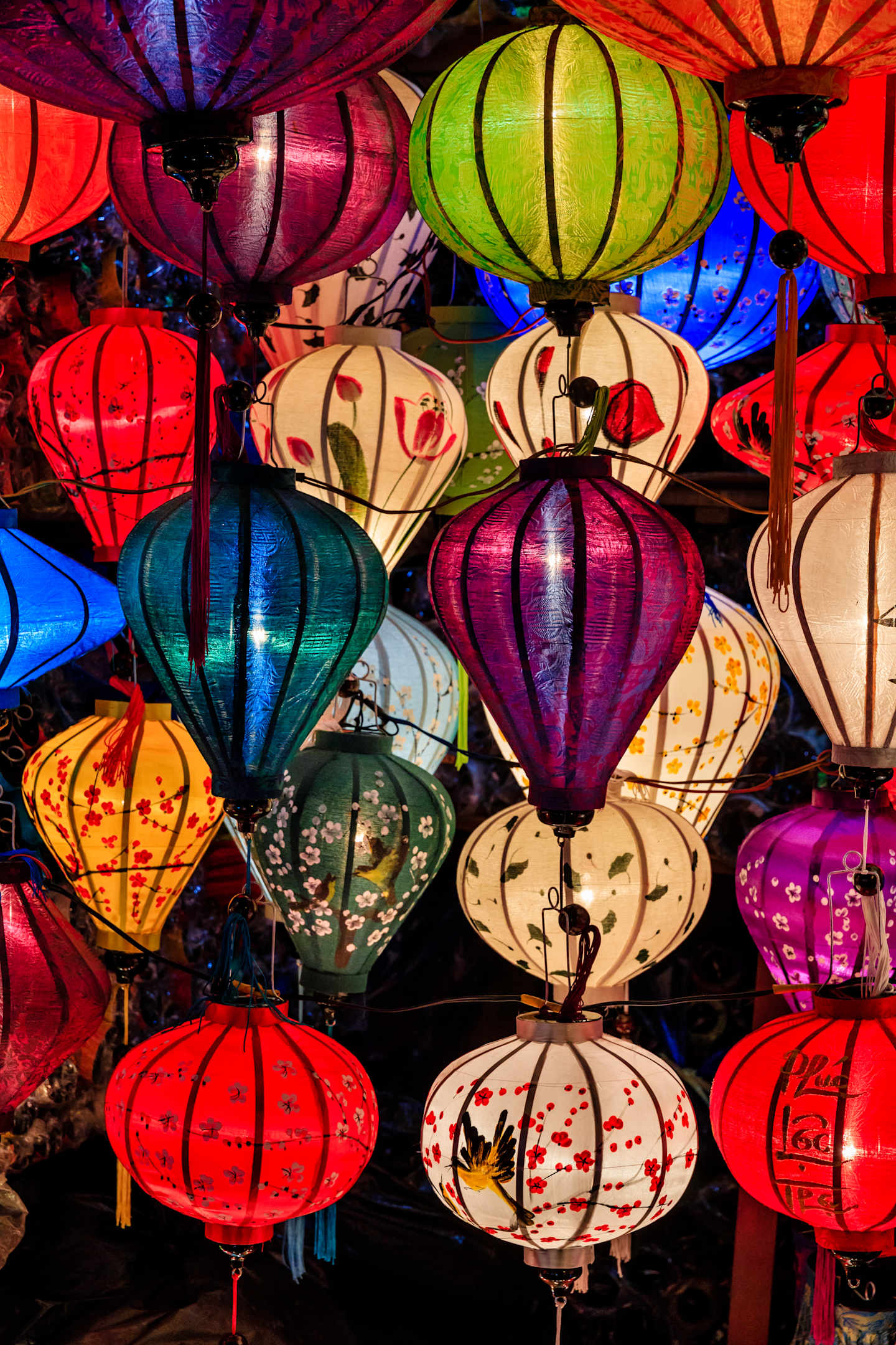 Vibrant and colorful lanterns of various shapes and sizes hang in a dimly lit setting, creating a captivating and festive atmosphere.