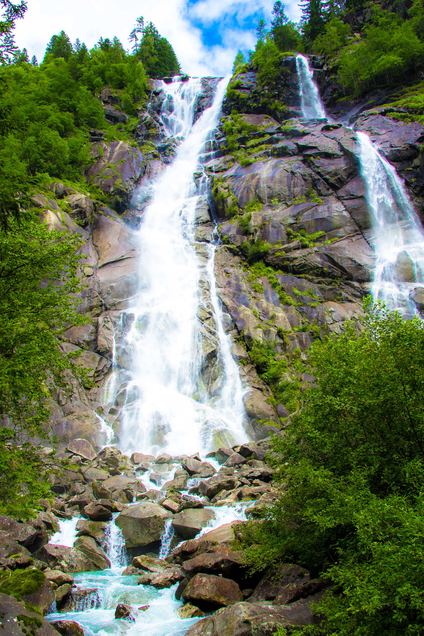 A majestic waterfall cascades down a rocky cliff, surrounded by lush green foliage and a clear blue sky in the background.