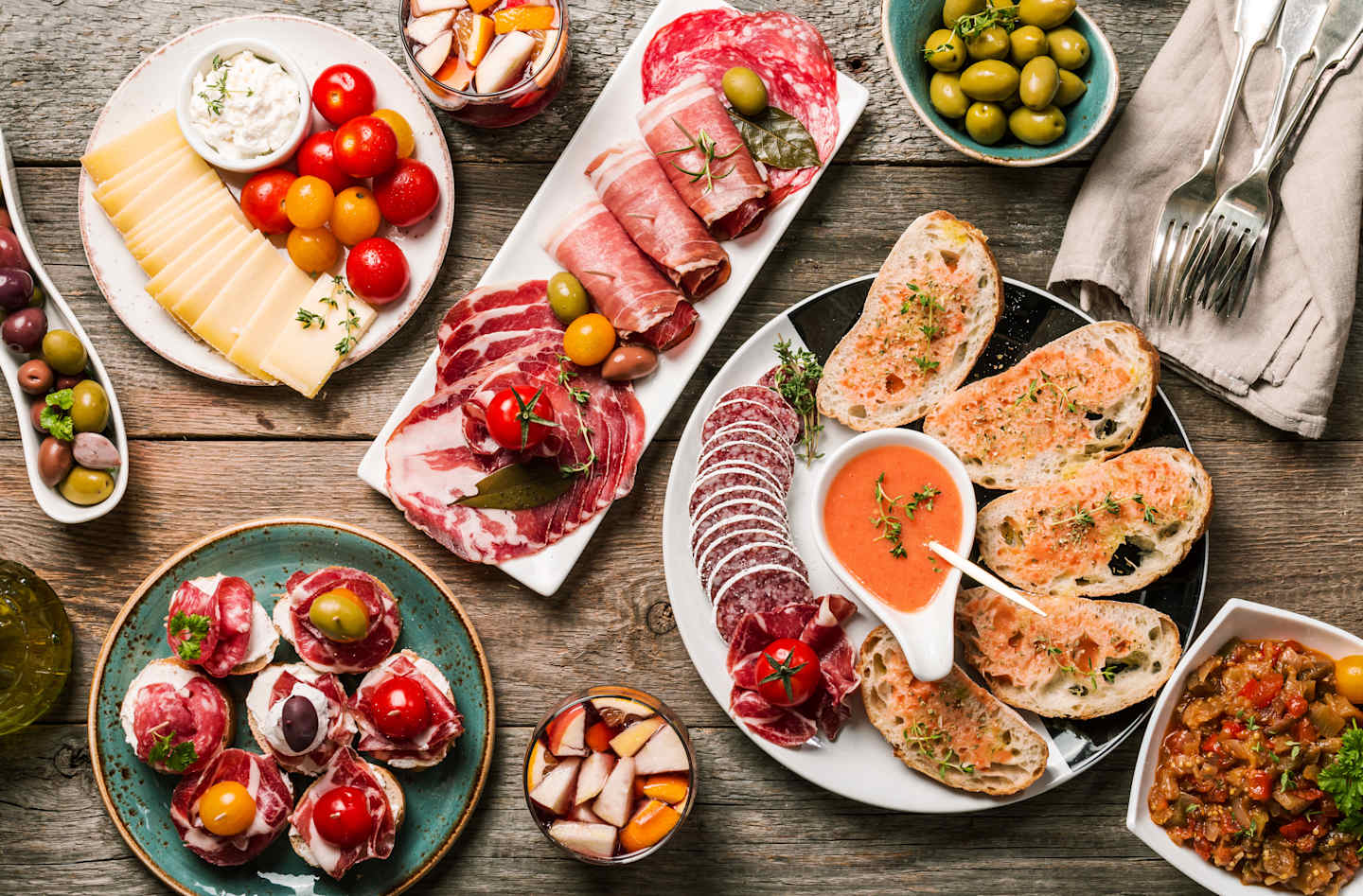 A variety of Italian appetizers and antipasti, including cured meats, cheeses, olives, and bread, arranged on a rustic wooden table.