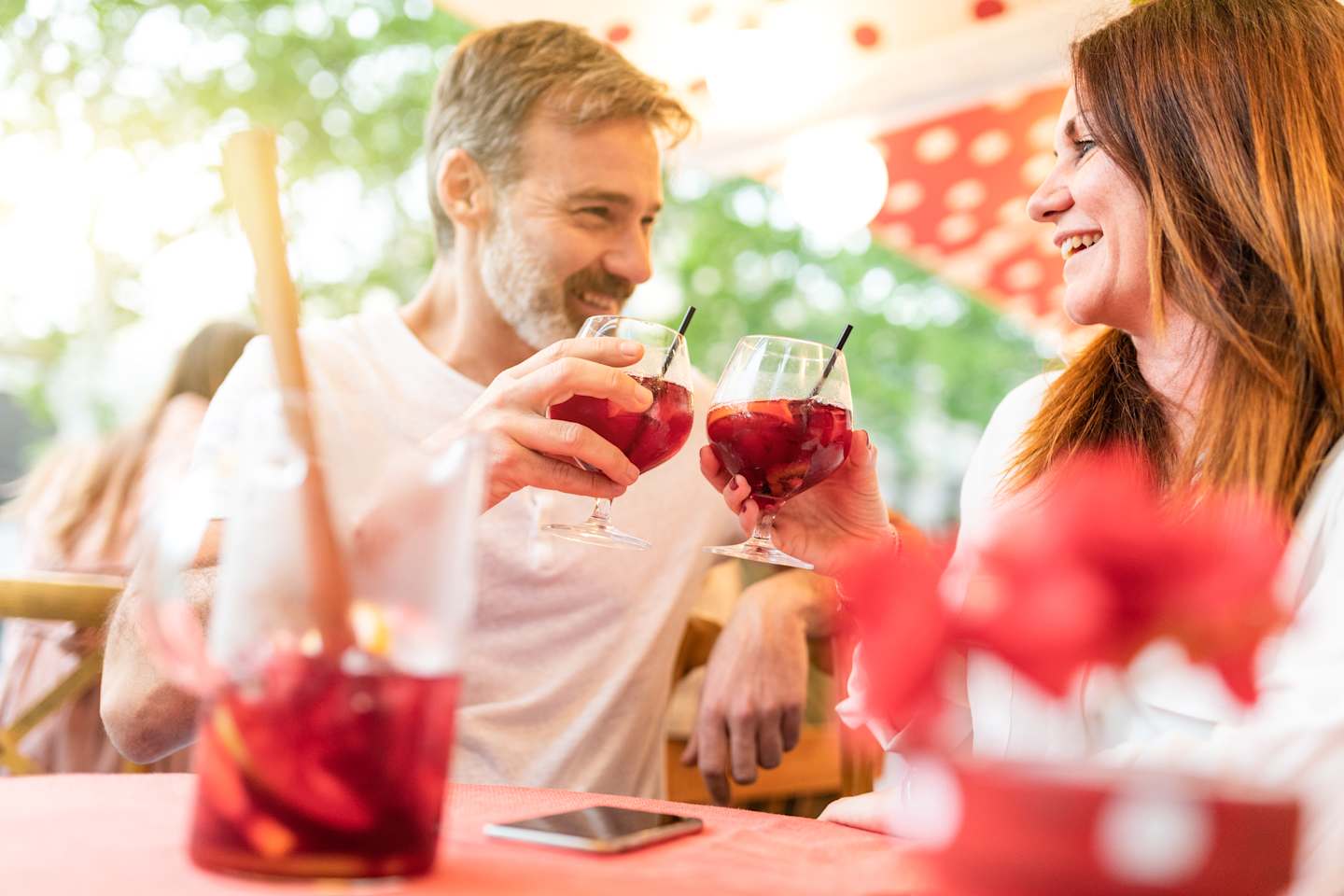 A smiling couple enjoying drinks together outdoors, surrounded by a lush, vibrant garden setting.