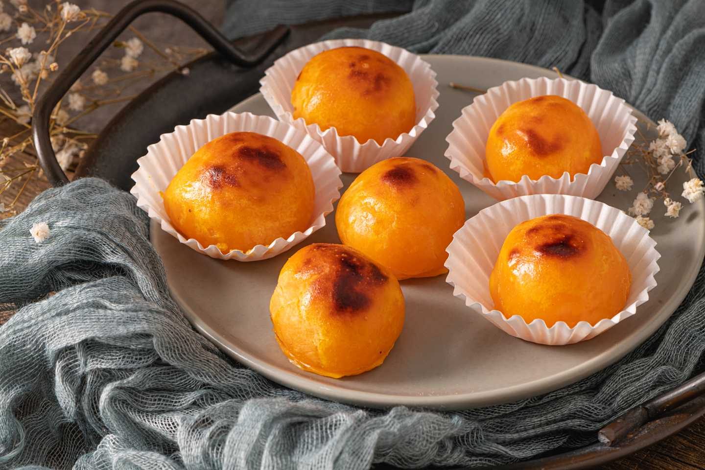 The image shows a plate filled with several golden-brown baked goods, likely pastries or desserts, arranged on a gray cloth or fabric in the background.