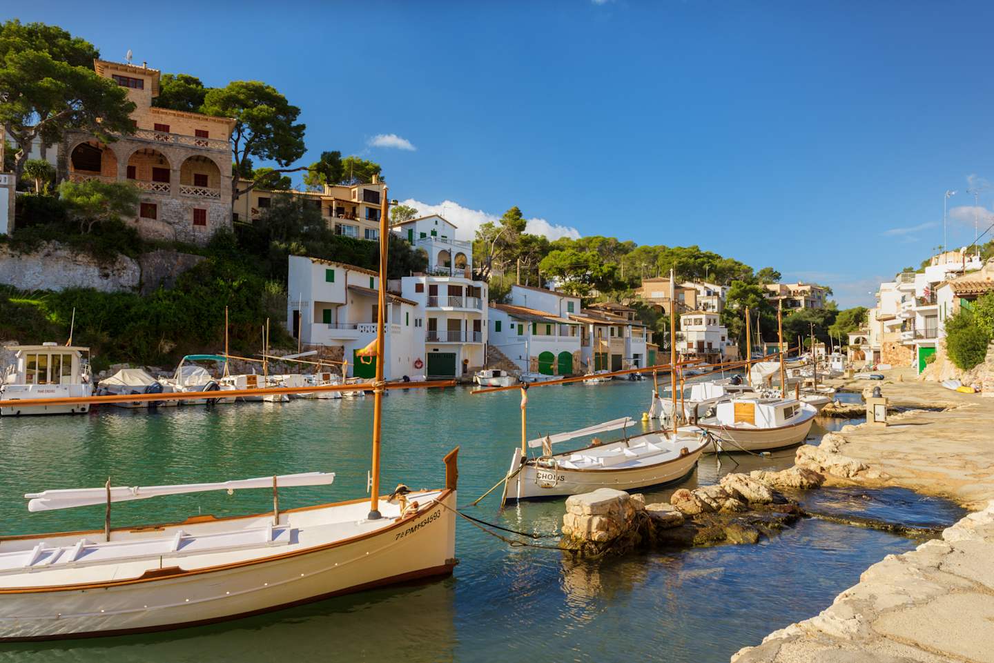 A picturesque harbor with colorful buildings, boats, and a serene body of water surrounded by lush greenery and a clear blue sky.