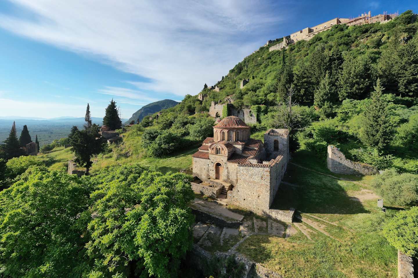 A medieval castle perched atop a lush, green hillside, surrounded by a picturesque landscape with mountains in the distance.