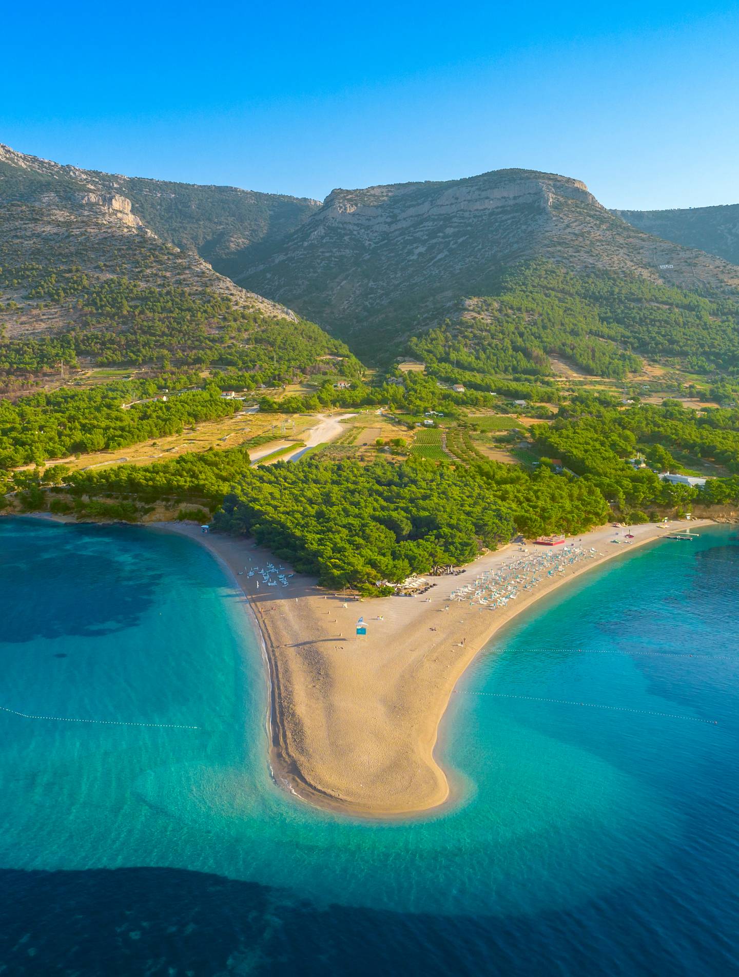 A stunning coastal landscape with a pristine sandy beach, crystal-clear turquoise waters, and lush green hills and mountains in the background, creating a picturesque and serene scene.