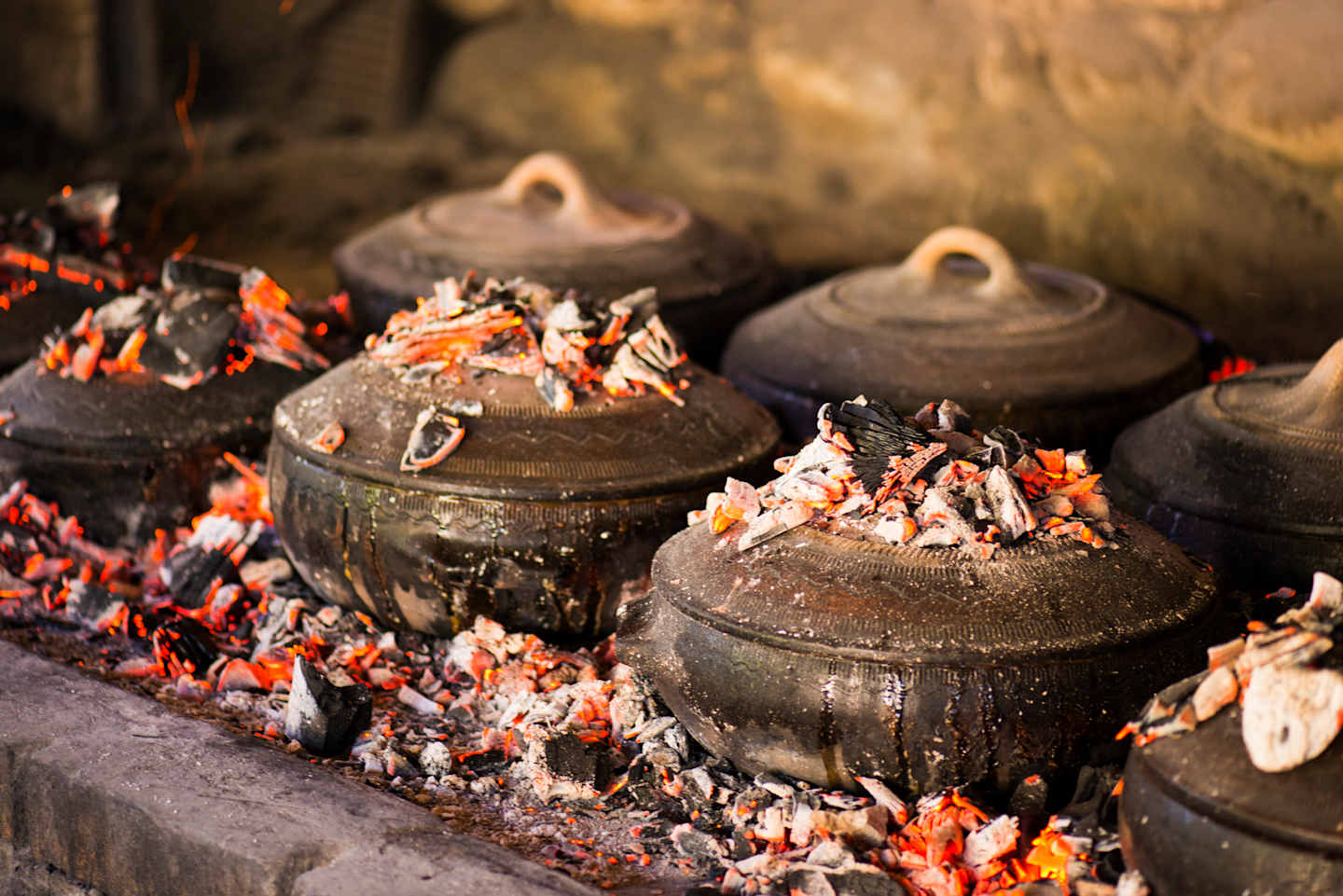 Rustic clay pots sit amidst glowing embers and scattered petals, creating a warm and earthy scene.