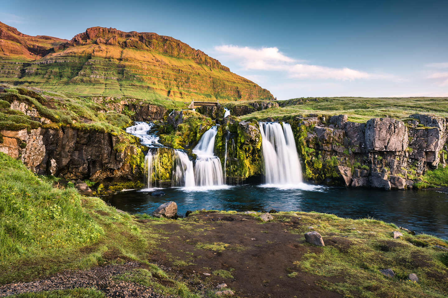 Majestic waterfalls cascade into a serene pool surrounded by lush, verdant cliffs and a clear blue sky.